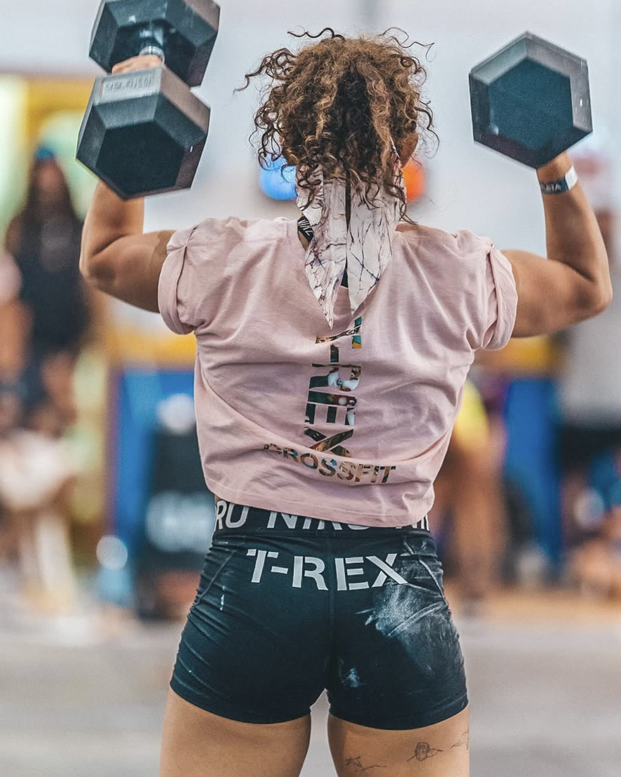 Raquel Sánchez levantando dos mancuernas por encima de la cabeza, de espaldas, con la camiseta de CrossFit T-Rex