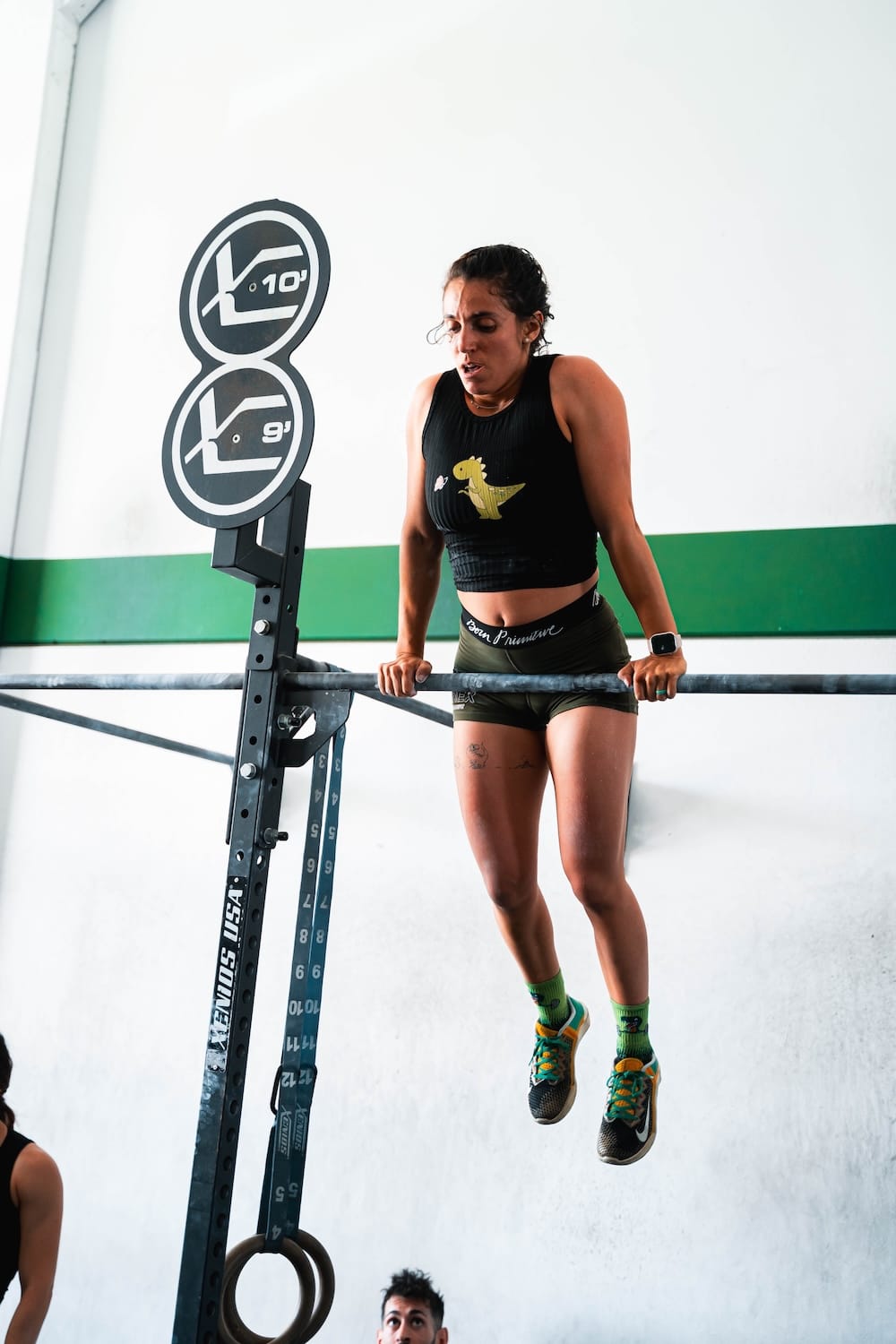 Una socia terminando un muscle-up en la barra, con la camiseta del box