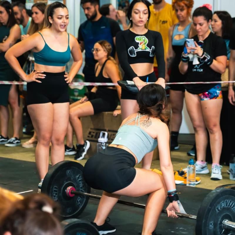 Una socia levantando peso muerto rodeada de compañeras animando